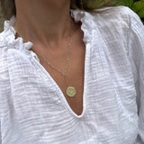 Gold necklace with a pendant on a person wearing a white top.