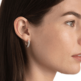 Close-up of a woman wearing a gold hoop earring with a clear gemstone.