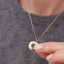 Gold necklace with a mountain pendant held by a hand against a gray sweater background