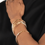 Close-up of a hand wearing multiple gold bracelets on a black background