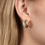 A close-up of a model's ear wearing a gold huggie hoop earring with a textured, pavé-set silver front.