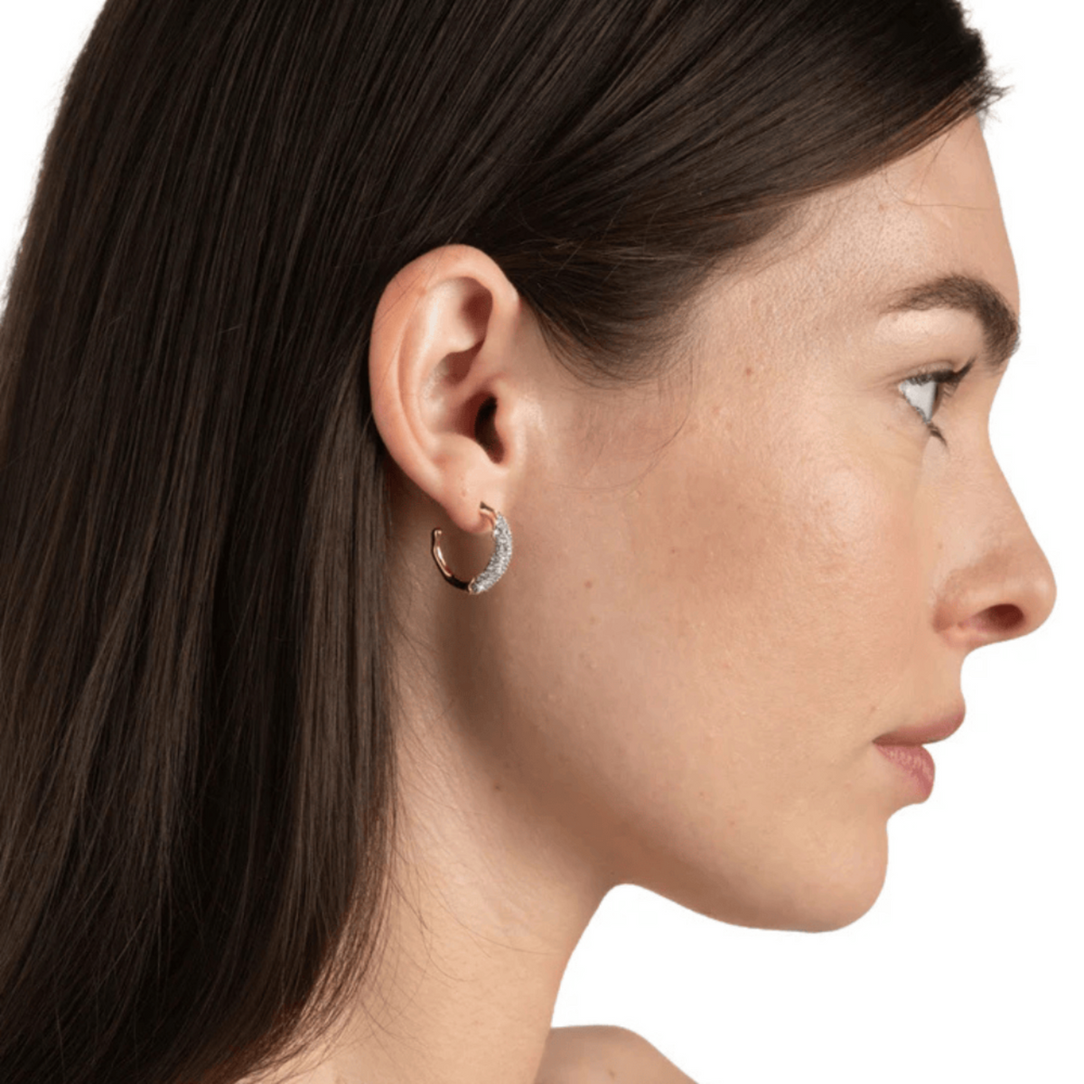 Close-up of a woman wearing a diamond hoop earring on a white background