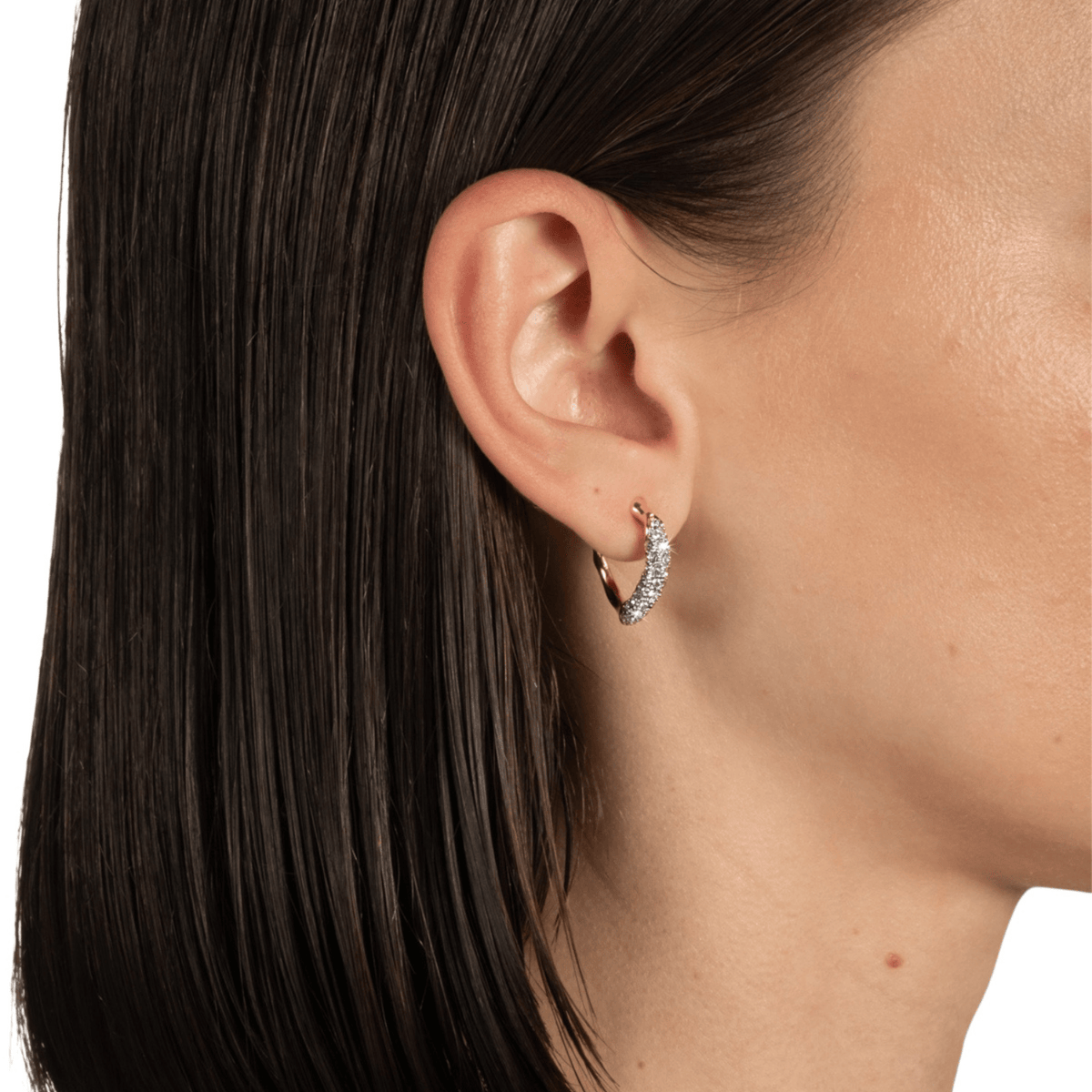 Close-up of a person wearing a gold hoop earring with small diamonds.