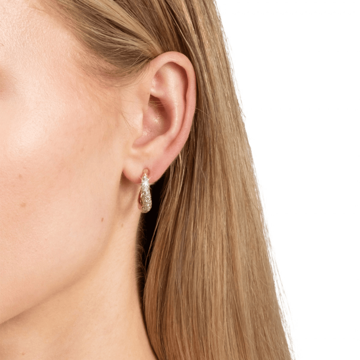 A close-up of a woman's ear wearing a small teardrop-shaped drop earring with a textured rose gold setting and clear stones, against a plain white background.