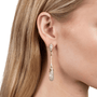 A close-up of a model's ear wearing a gold and silver drop earring with clear gemstones, set against a clean white background.