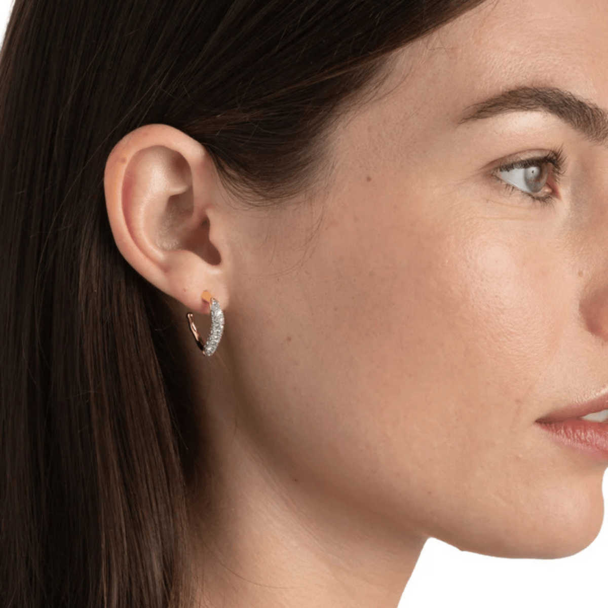 Close-up of a woman wearing a gold hoop earring with a clear gemstone.