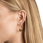 A close-up of a model's ear wearing a pair of gold hoop earrings