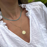 Close-up of a person wearing a gold necklace with a round pendant on a white background