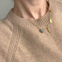 A close-up of a person wearing a delicate gold necklace with a small gray stone pendant and a tiny gold charm, styled over a beige knit sweater.