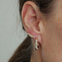 A close-up of a person's ear wearing a gold ear cuff adorned with small clear stones and a matching dangling hoop earring.