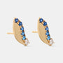 A pair of gold crescent-shaped stud earrings decorated with a row of faceted blue gemstones and a small clear stone at the tip, shown on a light gray background.
