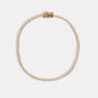 A delicate gold tennis necklace with small clear stones along the chain, displayed in a circular shape on a light gray background.