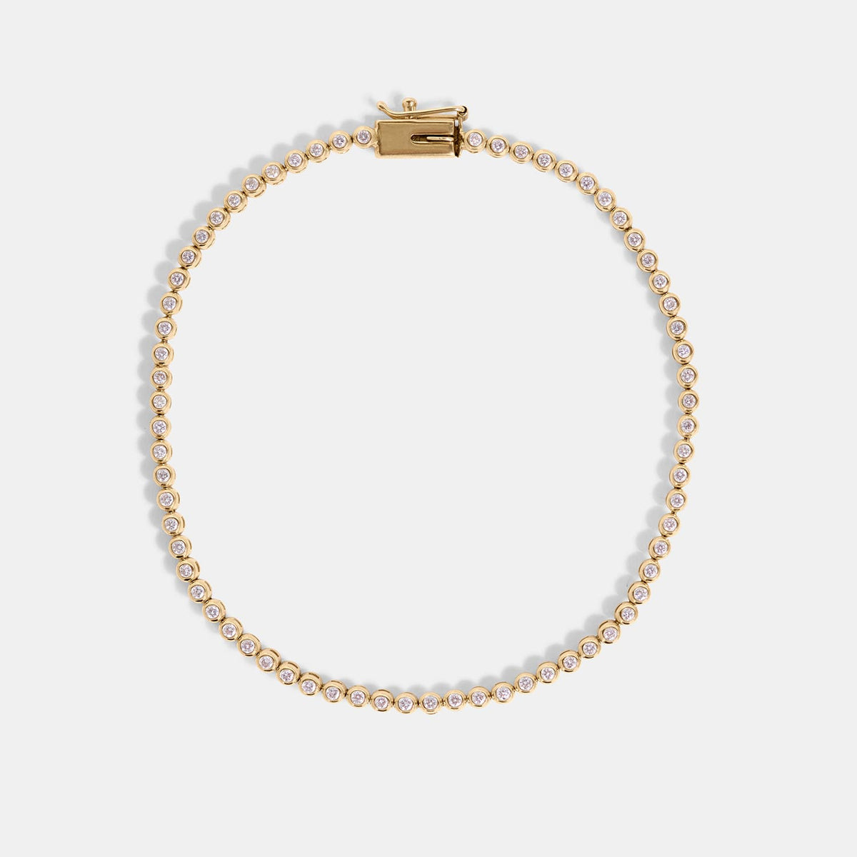 A delicate gold tennis necklace with small clear stones along the chain, displayed in a circular shape on a light gray background.