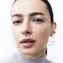 Close-up portrait of a woman wearing large gold hoop earrings and light blue-gray eyeshadow, against a clean white background.