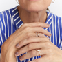 A close-up of a woman's hands wearing two delicate wavy rings, one in yellow gold and one in silver, with a blue and white striped shirt in the background.