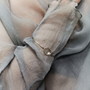 A close-up of a delicate gold ring bangle with a small white pearl, worn on a wrist covered by a sheer, textured gray-blue fabric.