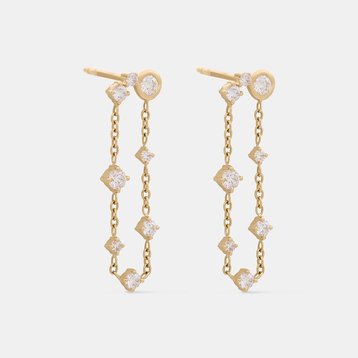 A pair of gold drop earrings with multiple clear gemstones set in a vertical chain design, photographed on a light gray background.