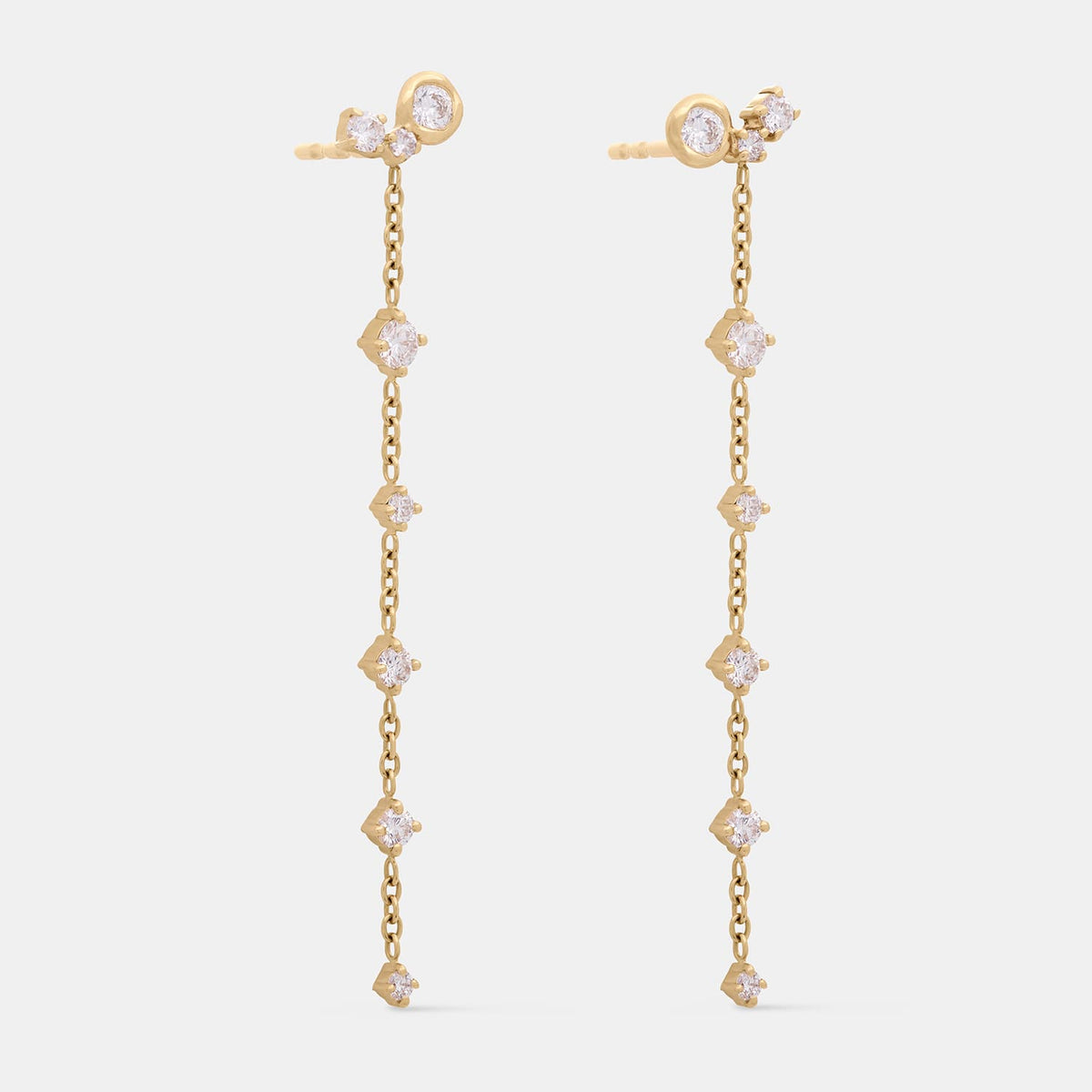 A pair of gold dangle earrings with clear gemstones, shown against a light gray background.
