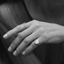 A close-up black and white photograph of a person's hand wearing two silver rings, with one ring featuring a large oval face and the other a delicate twisted band.