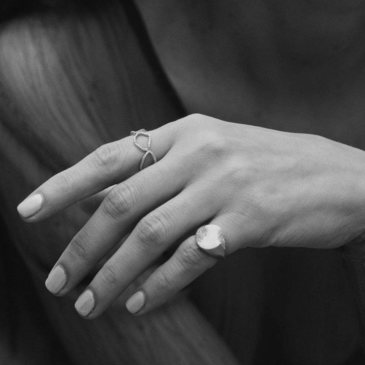 A close-up black and white photograph of a person's hand wearing two silver rings, with one ring featuring a large oval face and the other a delicate twisted band.