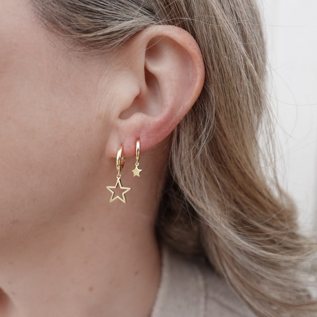 Close-up of a person wearing gold star-shaped earrings with a neutral background