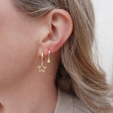 Close-up of a person wearing gold star-shaped earrings with a neutral background