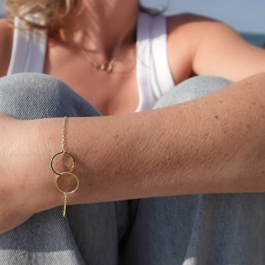 Close-up of a person's arm wearing a gold bracelet with interlocking rings.