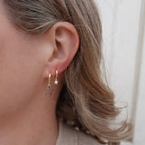 Close-up of a person wearing gold hoop earrings with star-shaped ends.