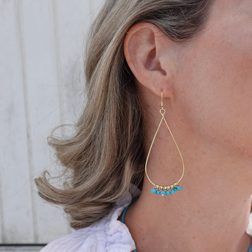 Gold teardrop earring with blue beads worn by a person with light brown hair.